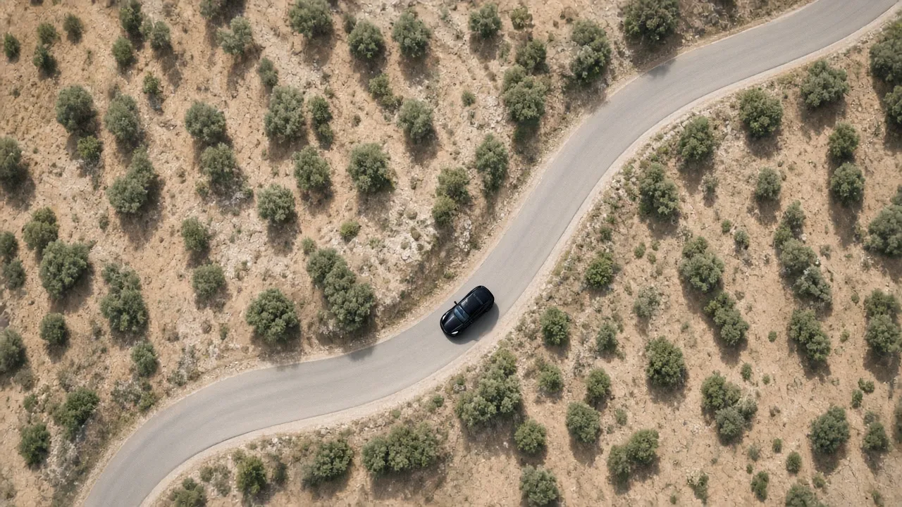 A black car from above on a winding road through dry hills and olive trees